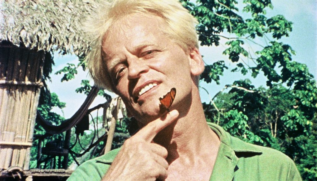 Klaus Kinski verträumt mit einem Schmetterling, der auf seinem Finger sitzt.