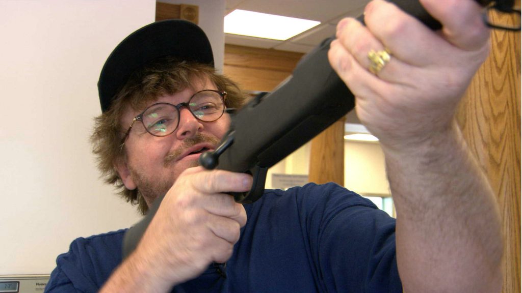 Michael Moore hält ein Gewehr.